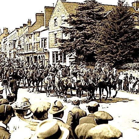 Crowd gathered as horse riders pass through a town street in a historic scene.