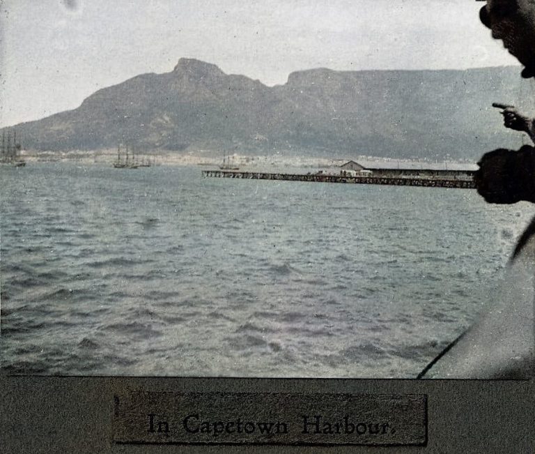 View of a harbour with mountains in the background and a pier extending into the water.