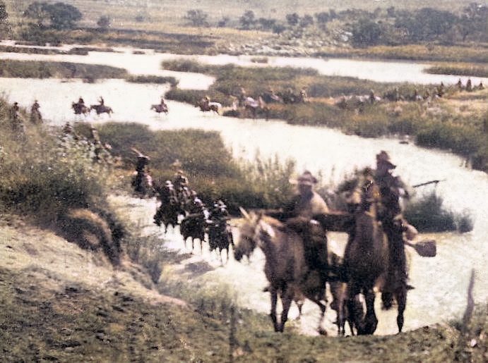 A group of horse riders navigating a marshy landscape near a river.