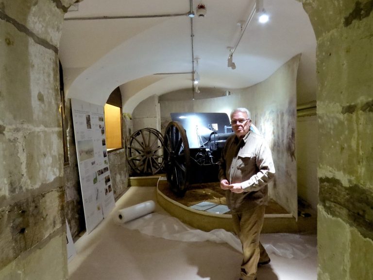 A man stands in a museum gallery near a large historical cannon.