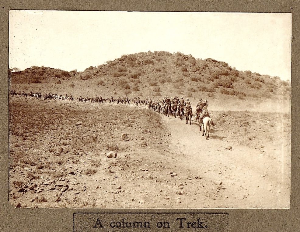 A line of cavalry trekking along a dusty path in a hilly landscape.