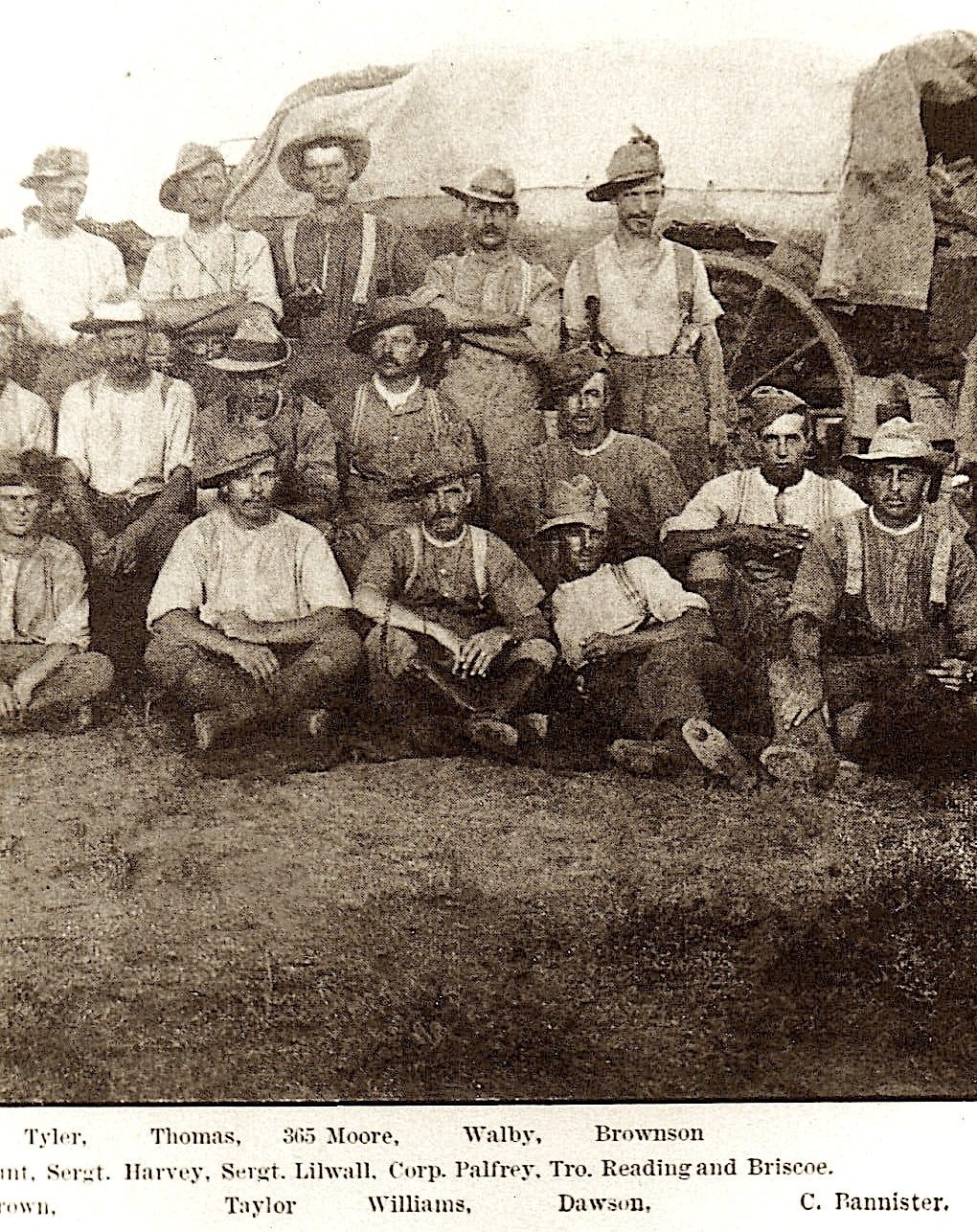 A group of men seated and standing outside a wagon in dirty rough military uniform.
